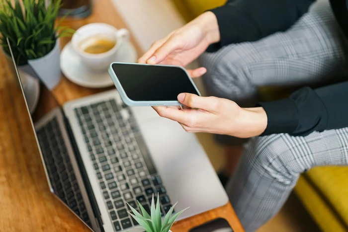 Gros plan de mains d'une personne envoyant un message avec son téléphone devant son ordinateur
